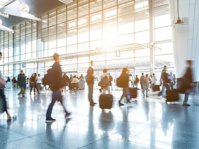 Grupo de personas en el aeropuerto caminando por el pasillo central con sus maletas, algunos buscan la salida, otros esperan, otros buscan su vuelo.