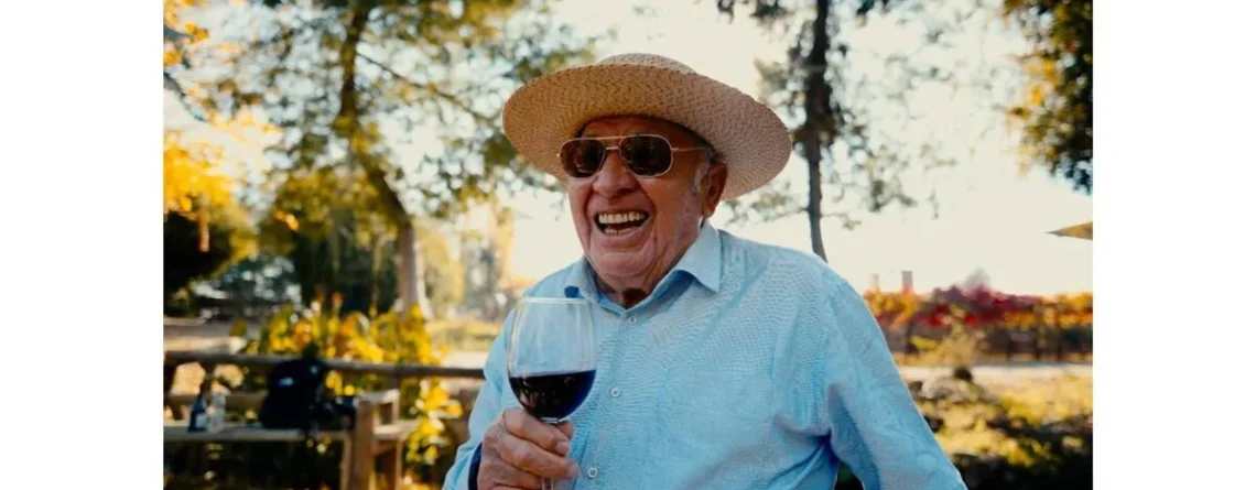 Don Raúl Ravanal, patriarca fundador del Hotel Cava Colchagua en Santa Cruz, sostiene una copa de vino de su viña que es parte de Hotel, él a trabajado este ensamblaje y sonríe a posando cerca de la laguna
