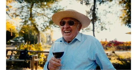 Don Raúl Ravanal, patriarca fundador del Hotel Cava Colchagua en Santa Cruz, sostiene una copa de vino de su viña que es parte de Hotel, él a trabajado este ensamblaje y sonríe a posando cerca de la laguna