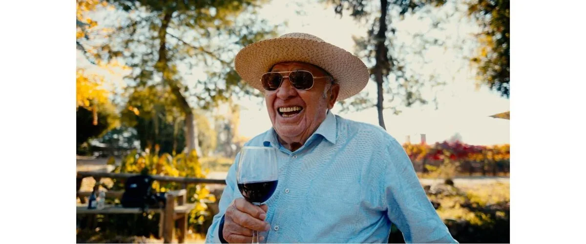 Don Raúl Ravanal, patriarca fundador del Hotel Cava Colchagua en Santa Cruz, sostiene una copa de vino de su viña que es parte de Hotel, él a trabajado este ensamblaje y sonríe a posando cerca de la laguna