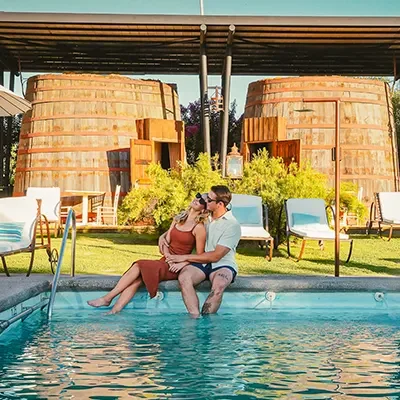Mujer y hombre felices disfrutan de la piscina en el Hotel Cava Colchagua, con las barricas de habitación de fondo.